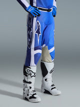 Alpinestars 2026 Racer Air Portl Pants, Motocross Pants, Ucla Blue and White, worn with matching blue gloves and white and black motocross boots, featuring large white Alpinestars logos, tan leather inner knee panels, and a black magnetic waist buckle.