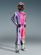 Motocross rider wearing Alpinestars 2026 Racer Air Portl Pants in Multicolor, featuring a vibrant pink, purple, and orange gradient design, paired with a matching jersey, white and black motocross boots, and a coordinating helmet with yellow goggles, complete off-road racing gear.