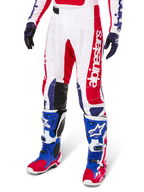 Alpinestars Limited Edition Techstar Fortitude Pants, Motocross Pants, Bright Red White and Blue, worn with matching off-road boots and gloves, featuring vertical branding on the leg, breathable perforated panels, and black reinforced knee sections, athletic race fit design