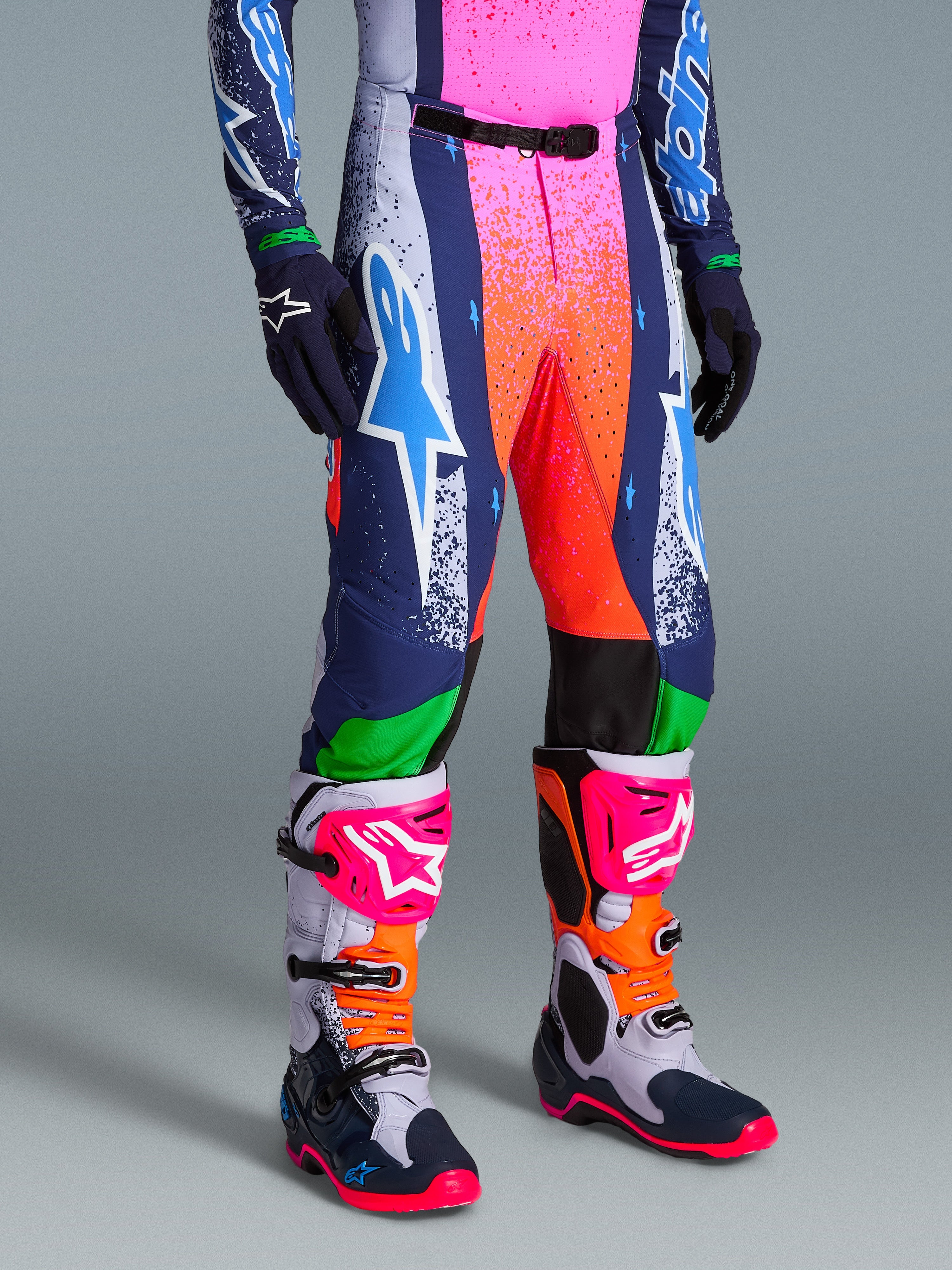 Alpinestars Limited Edition Supertech Records Pants, vibrant multicolor motocross pants with splattered pink and orange graphics, navy blue and white panels, featuring a large white and cyan Astars logo, worn with coordinating performance boots and gloves.