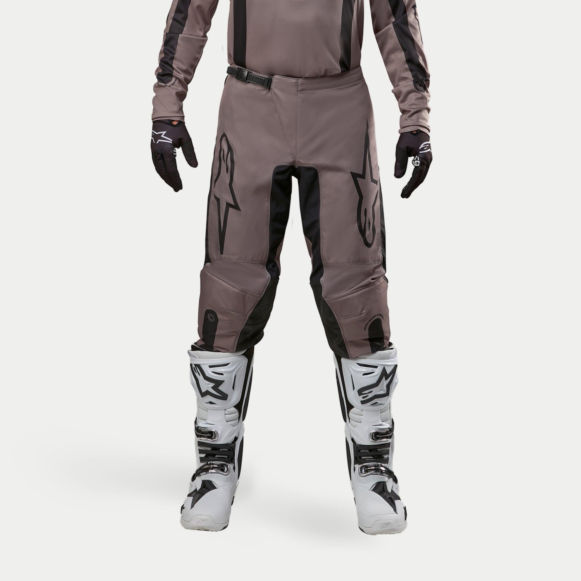 Alpinestars 2024 Fluid Lurv Pants, Motocross Pants, Mud Black, worn with matching jersey, black gloves, and white boots, featuring large black logos on thighs, ergonomic fit, and durable material for off-road racing