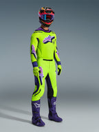 Motocross rider wearing the 2026 Supertech Vista Jersey, Bright Yellow with purple and black accents, matching yellow motocross pants, purple boots, and yellow gloves, multicolored helmet with blue goggles, high-performance racing gear for off-road competition