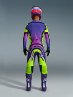 Alpinestars 2026 Supertech Vista Gear Set, back view of a motocross rider wearing a vibrant purple, pink, and lime green gradient racing outfit, featuring matching jersey and pants with bold branding, coordinated purple and pink helmet, purple boots, and black gloves.
