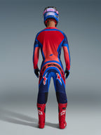 Alpinestars 2026 Supertech Vista Pants, Motocross Pants, Dark Navy Hot Coral and Cobalt, rear view of a rider in complete racing gear including matching jersey, blue helmet, and red boots, featuring bold branding on the seat and legs.