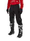 Alpinestars Techdura Pants, Black off-road motorcycle pants, worn with a red long-sleeve jersey and black and white motocross boots, featuring rugged stretch polyamide construction, leather inner knee reinforcements, and an adjustable buckled belt for enduro riding.