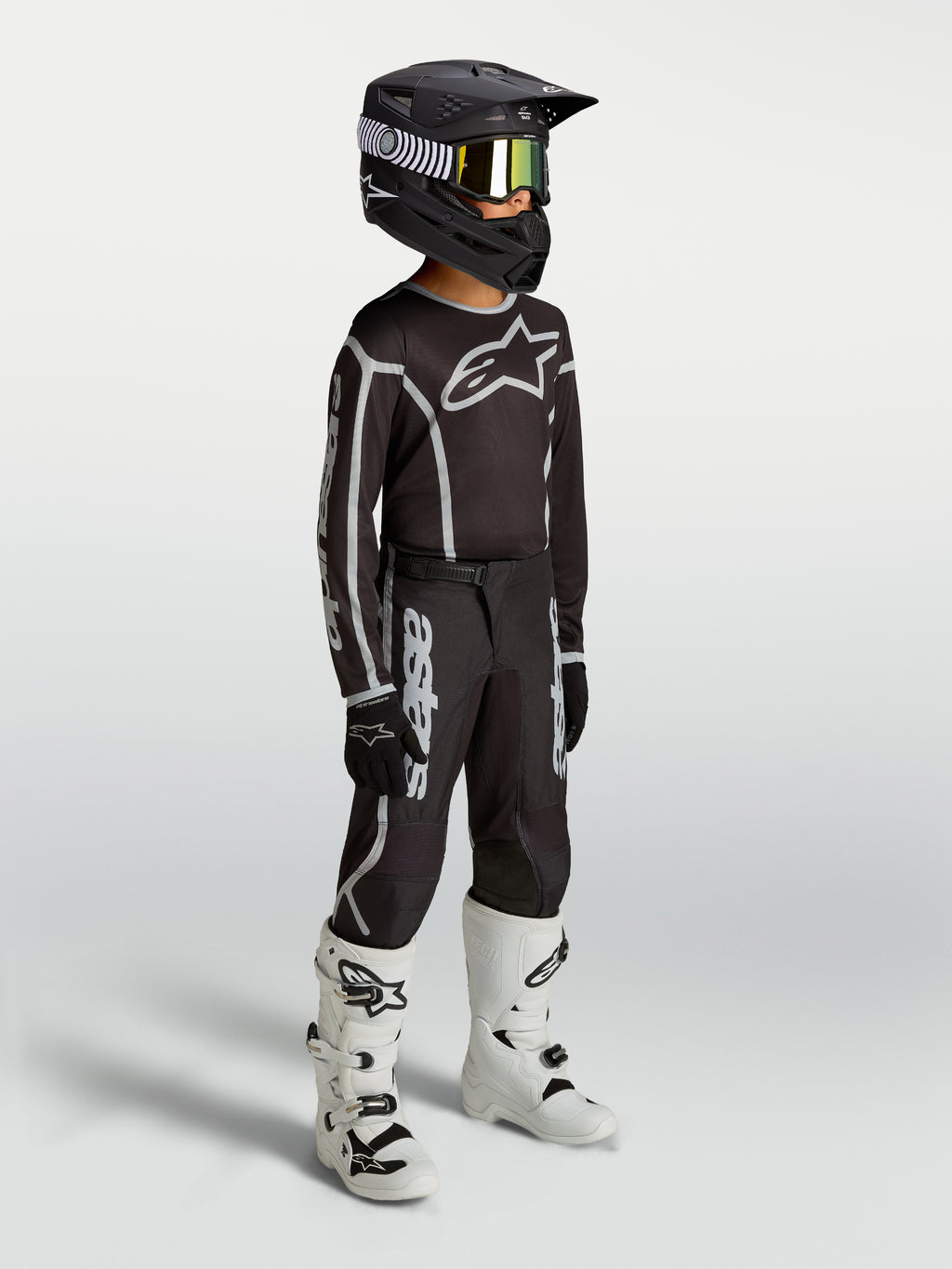 Alpinestars Youth Fluid Apex V2 Pants, black and silver motocross gear shown on-model with jersey, helmet, and white boots.