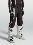 Alpinestars Youth Fluid Apex V2 Pants, black and silver motocross gear for young riders, featuring an ergonomic pre-curved fit.