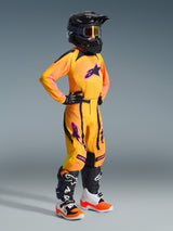 Youth motocross rider wearing complete racing gear, Orange jersey with pink Alpinestars logo, 2026 Youth Supertech Nomur Pants in Orange Yellow Pink, black helmet and goggles, white and black boots, black and white gloves, coordinated outfit for youth off-road racing