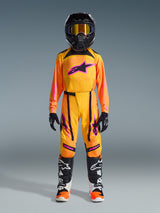 Youth motocross rider wearing the Alpinestars 2026 Youth Supertech Nomur gear set, Orange Yellow and Pink, featuring matching pants and jersey, black helmet with yellow goggles, and Alpinestars racing boots, complete professional outfit for off-road performance.