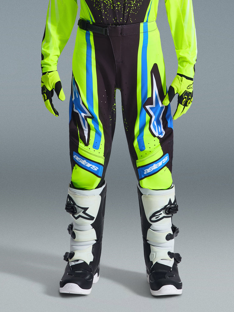 Alpinestars 2026 Youth Supertech Nomur Pants, Motocross Pants, Dark Navy, Yellow Fluo, and UCLA Blue, worn with matching gloves and black and white boots, featuring large star logos and 'astars' branding, professional-level gear for young riders