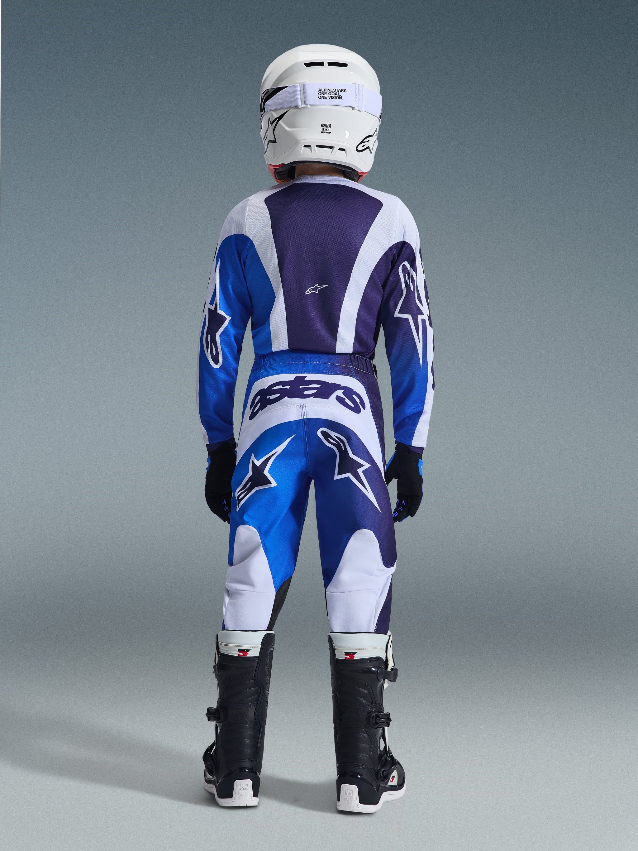 Alpinestars 2026 Youth Fluid Portl Pants, Motocross Pants, Ucla Blue and White, back view of a youth rider wearing a coordinated racing kit, featuring bold 'astars' branding on the rear and star logos on the legs, paired with matching jersey, white helmet, and black boots.