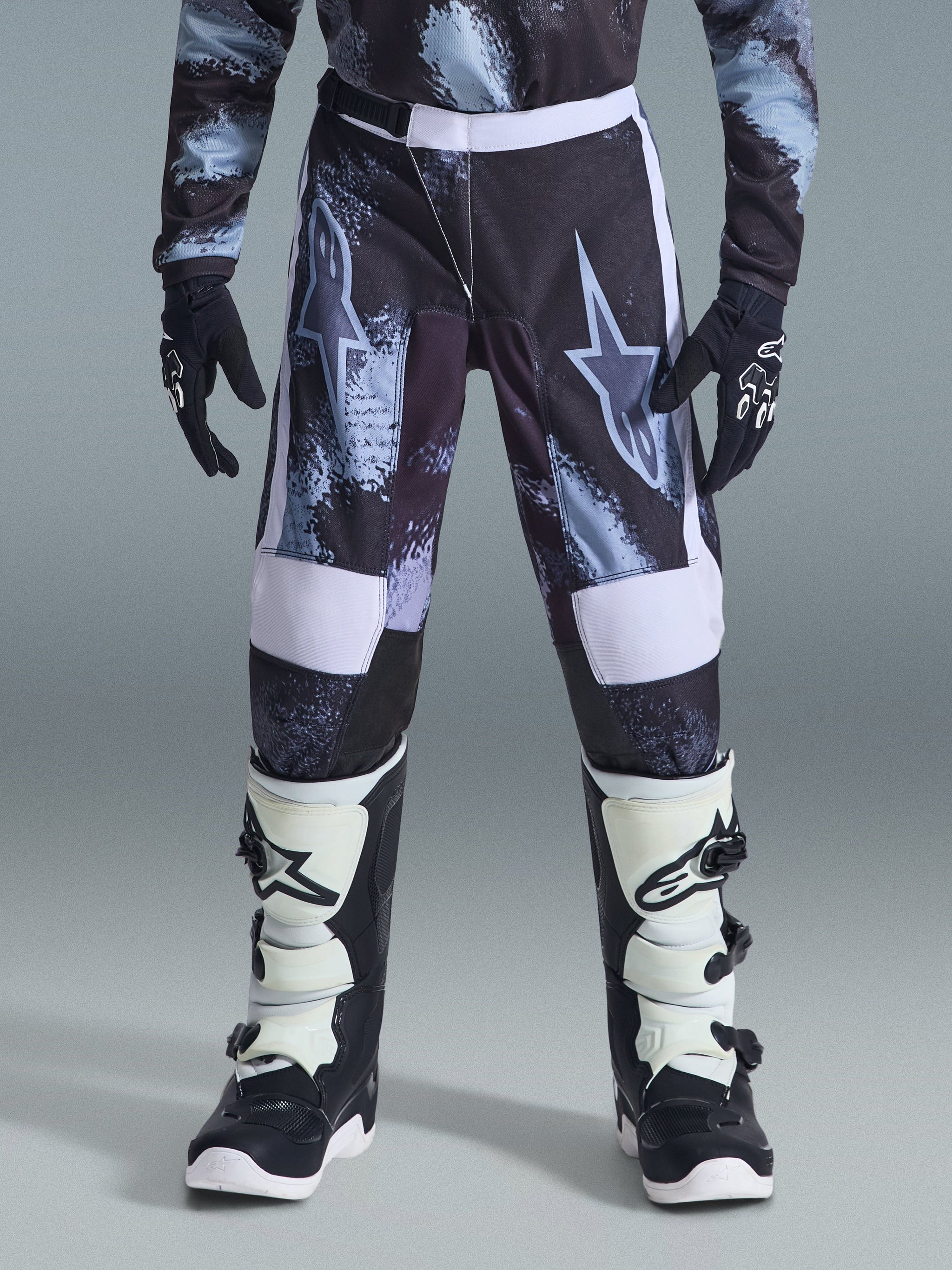Alpinestars 2026 Youth Fluid Lahnd Pants, Youth Motocross Pants, Iron Camo with white accents, worn with black and white off-road boots and gloves, durable design for young riders.