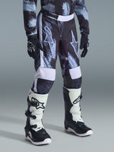 Alpinestars 2026 Youth Fluid Lahnd Pants, Motocross Pants, Iron Camo camouflage in grey, black, and white, worn with matching long-sleeve jersey, black racing gloves, and white and black motocross boots, featuring large star logos on the thighs.