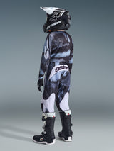 Alpinestars 2026 Youth Fluid Lahnd Pants, Motocross Pants, Iron Camo pattern, youth rider seen from behind wearing matching camo jersey, black and white boots, and black helmet, featuring white panels and 'astars' branding on the back, full gear set for off-road racing