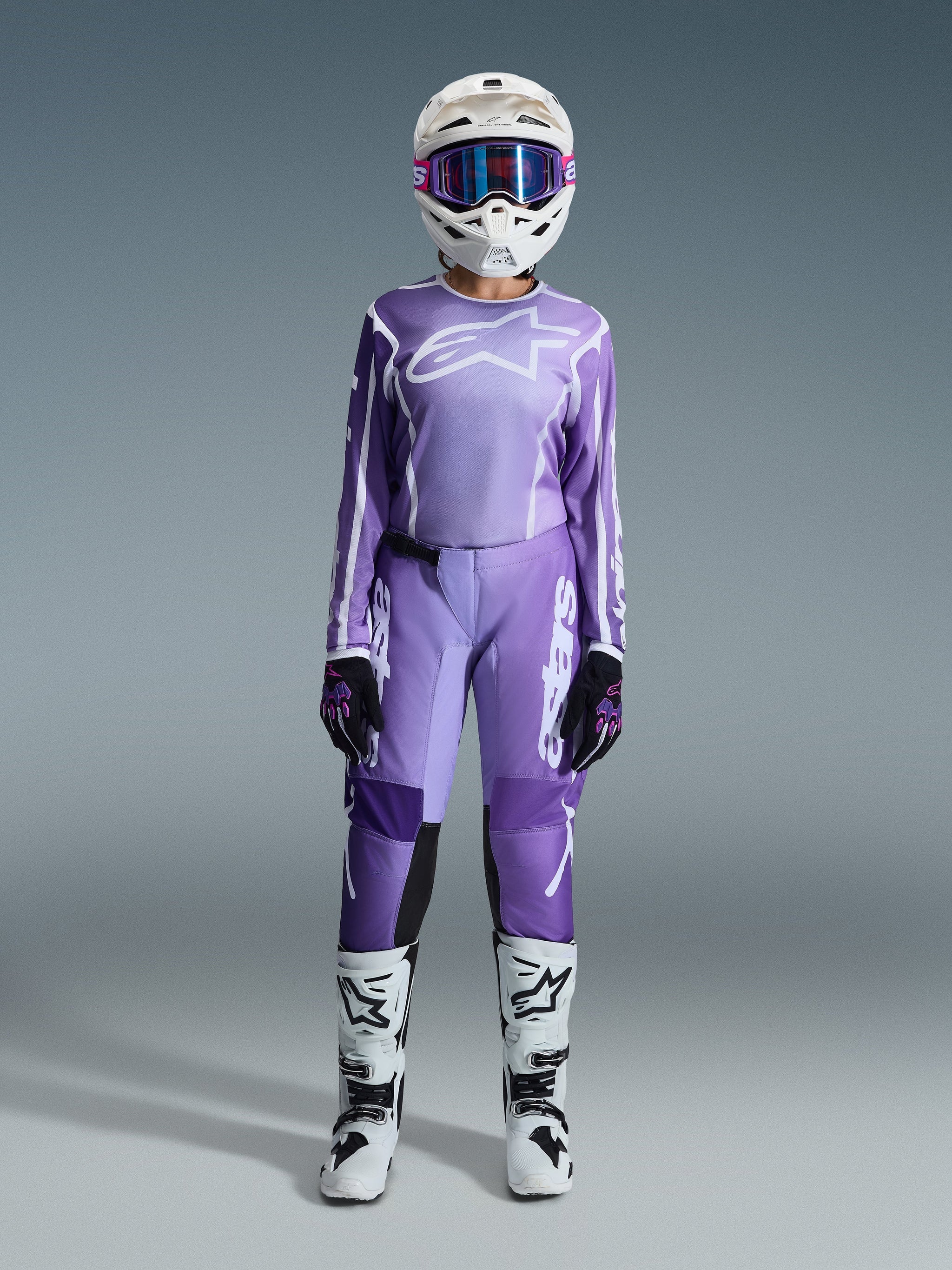 Alpinestars 2026 Stella Fluid Apex Pants, Motocross Pants, Violet and White, worn with matching long-sleeve jersey, white helmet with purple goggles, black and purple gloves, and white and black boots, complete coordinated racing outfit for women
