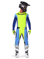 Motocross rider wearing complete racing gear, Alpinestars 2025 Techstar Melt Jersey in Yellow Fluo and Blue, matching yellow and blue motocross pants, black helmet with white graphics and goggles, white and black boots, yellow and black gloves, coordinated performance outfit for off-road racing
