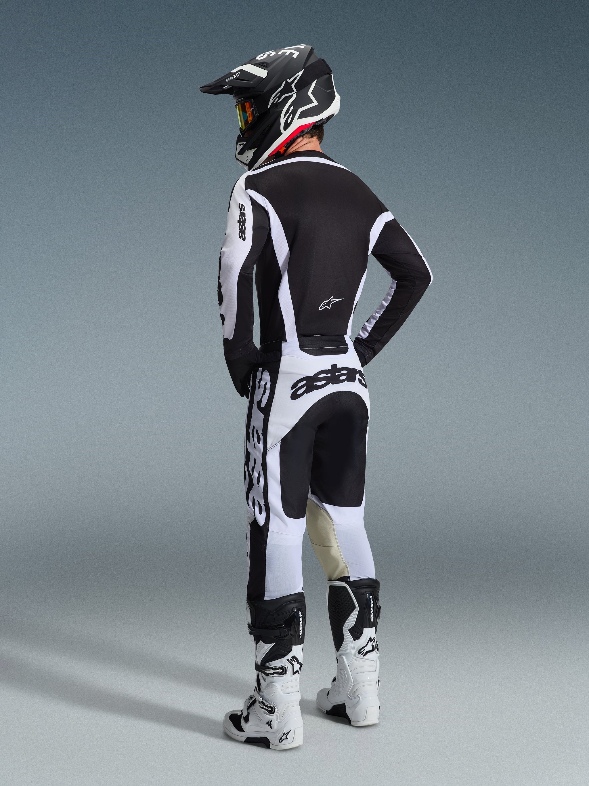 Motocross rider wearing complete racing gear from behind, White and Black Alpinestars 2026 Racer Riway Jersey, matching white and black pants with bold 'astars' branding, white boots, and a black helmet with white accents, coordinated performance outfit for off-road racing.