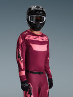 Motocross rider wearing Alpinestars 2026 Racer Riway Gear Set, Burgundy and Pink jersey with bold 'astars' branding, matching pants with pink accents, black helmet and gloves, professional racing outfit for off-road motocross