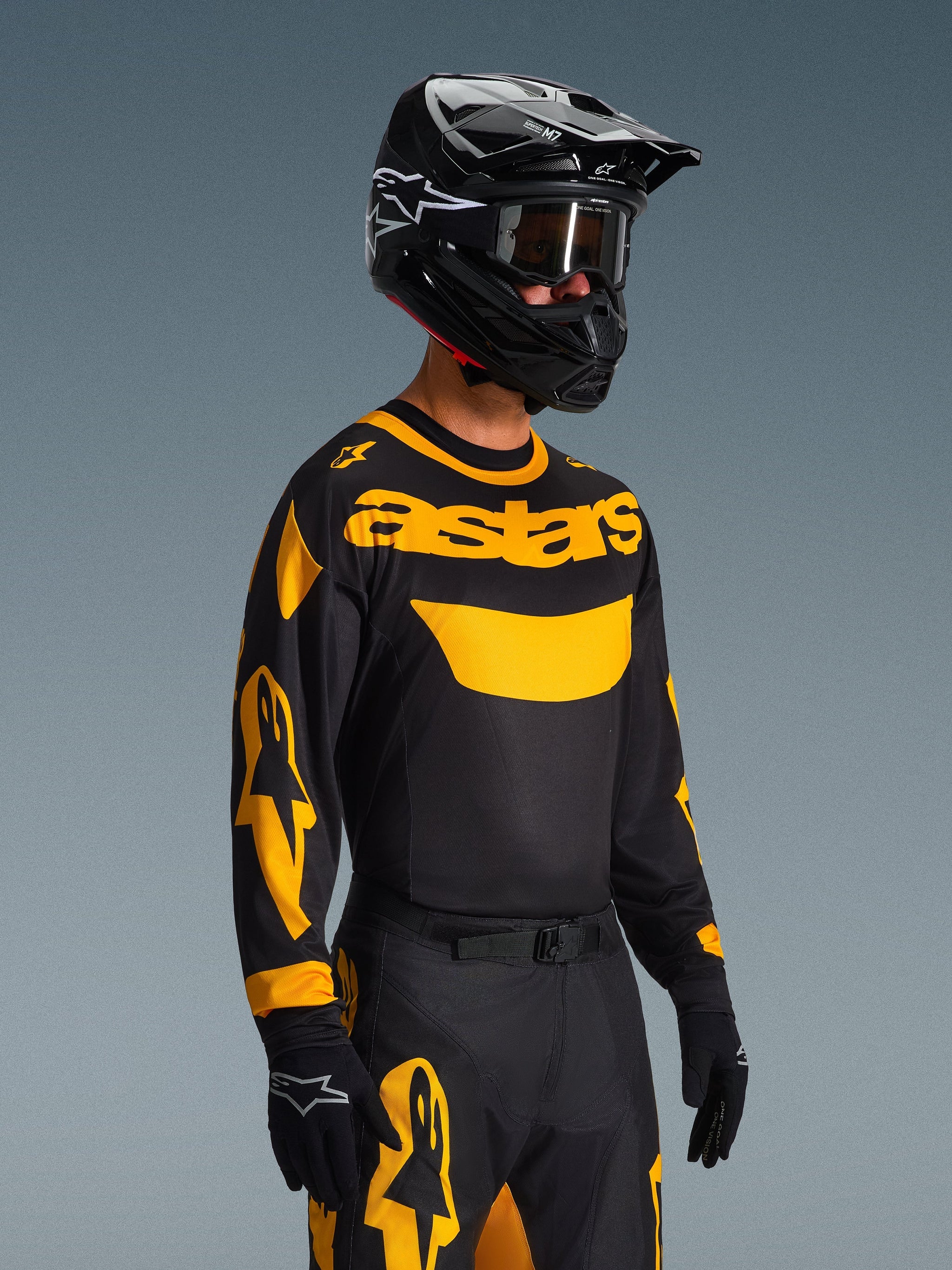 Motocross rider wearing the Alpinestars 2026 Racer Riway Jersey in Yellow and Black, black jersey with bold yellow 'astars' branding and sleeve graphics, matching black and yellow pants, black helmet with goggles, and black gloves, professional off-road racing kit