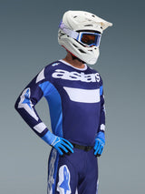 Motocross rider wearing the Alpinestars 2026 Racer Riway Jersey in UCLA Blue White, featuring 'astars' branding on the chest, paired with matching blue motocross pants, white helmet with goggles, and blue gloves, high-performance off-road racing gear