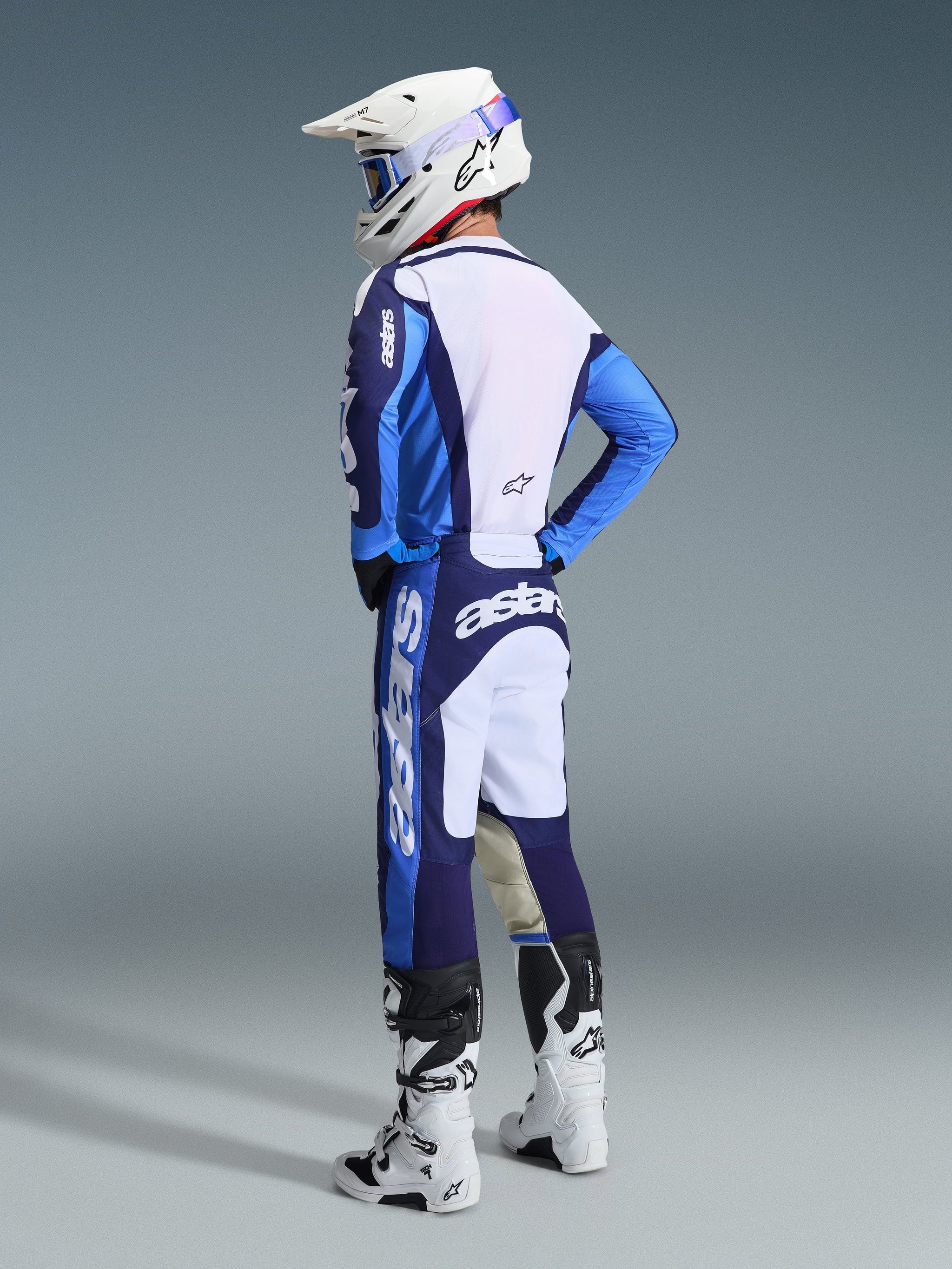 Motocross rider wearing the 2026 Racer Riway Jersey in Ucla Blue and White, paired with matching blue and white motocross pants, a white helmet, and white boots, shown from a back three-quarter view for a complete off-road racing look.