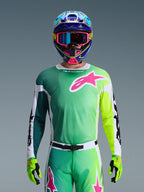 Alpinestars 2026 Racer Portl Gear Set, Motocross Rider wearing Green and Yellow gradient jersey with Pink Astars logo, matching pants, colorful blue and pink helmet with blue goggles, and lime green gloves, coordinated professional off-road racing outfit