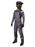 Motocross rider wearing Alpinestars 2025 Fluid Haul Gear Set in Gray, including gray jersey and pants with black accents, black helmet with reddish goggles, black gloves, and black boots with white logos, complete off-road racing outfit