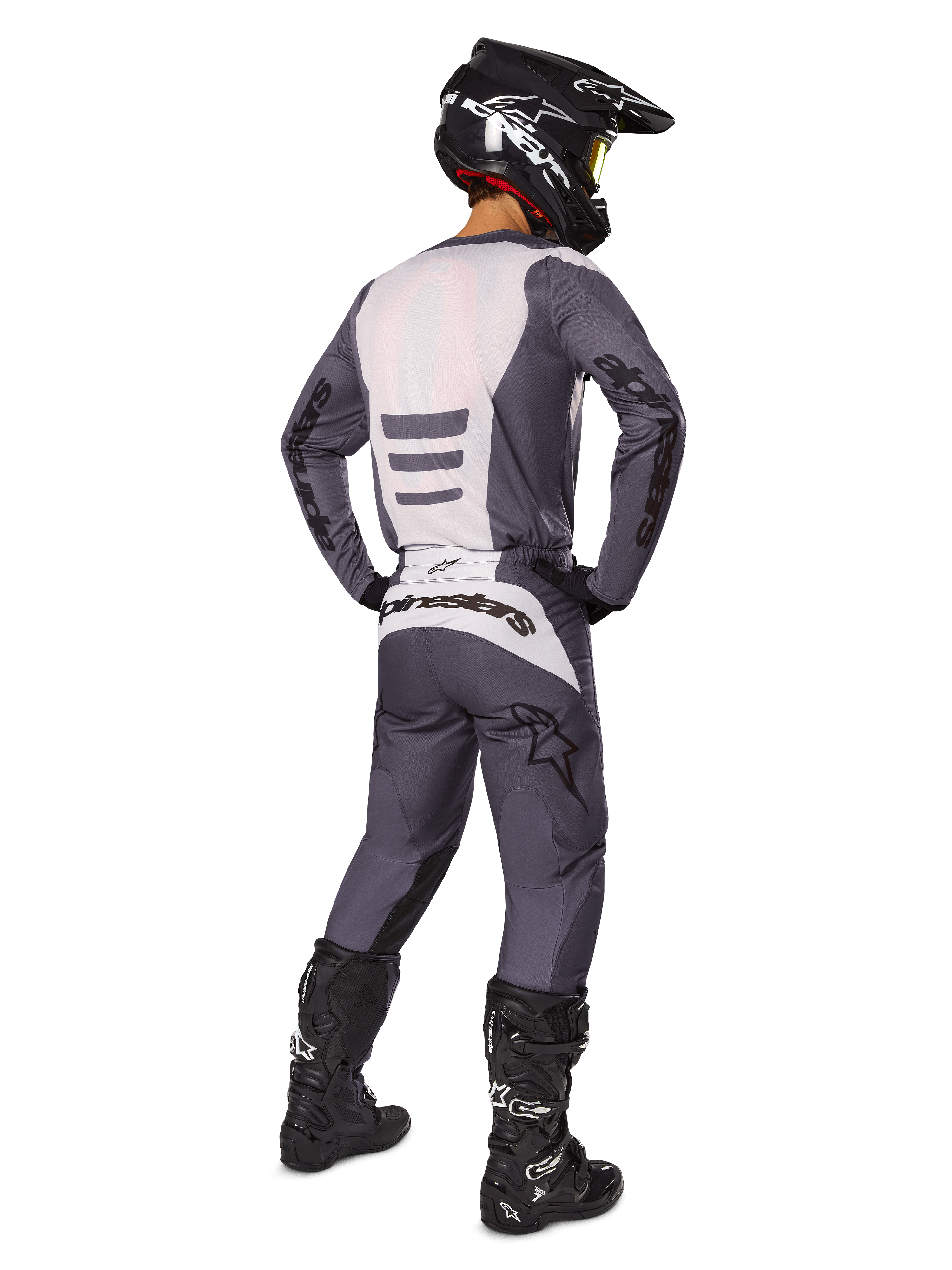 Motocross rider from the back wearing Alpinestars 2025 Fluid Haul Gear Set, Gray and White jersey and matching pants, black helmet with yellow goggles, black motocross boots, complete racing gear for off-road performance