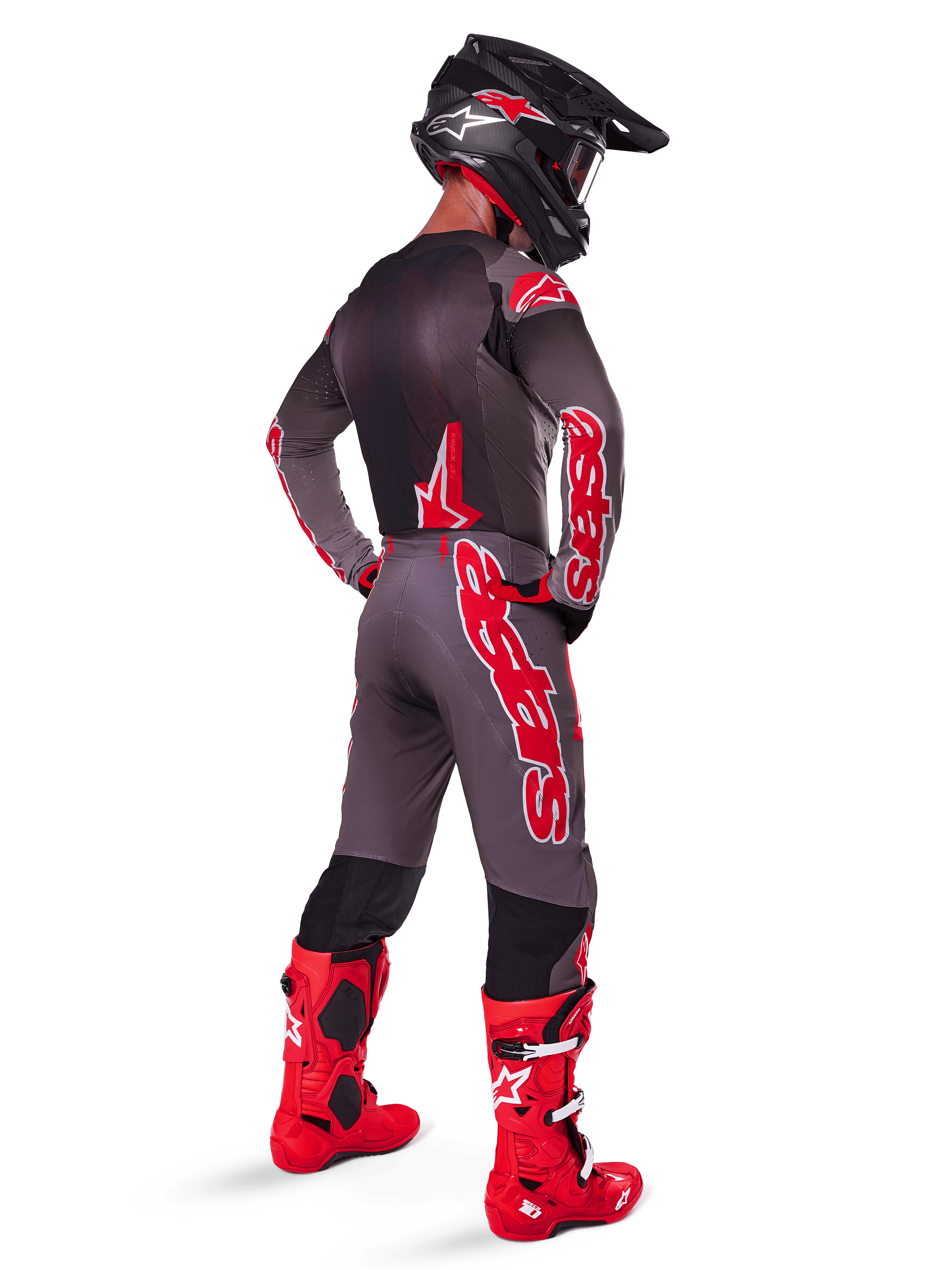 Motocross rider wearing the 2025 Supertech Lipan Gear Set in Smoke Bright Red, viewed from the back, featuring a grey jersey and matching pants with bold red Alpinestars branding, bright red racing boots, and a black helmet with red logos, complete professional off-road racing outfit