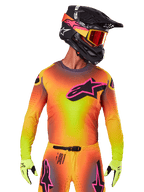 Motocross rider wearing the 2025 Supertech Lipan Jersey, vibrant yellow orange and pink gradient colorway, large black Alpinestars star logo with pink outline on the chest, laser-cut perforations for ventilation, athletic race fit, paired with matching pants, yellow gloves, and a black helmet with goggles.
