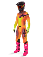 Motocross rider wearing the 2025 Alpinestars Supertech Lipan Gear Set, yellow and orange gradient jersey and pants with pink accents, black helmet with yellow-red goggles, bright yellow gloves, and vibrant pink boots, coordinated off-road racing outfit