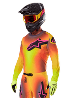 Motocross rider wearing the Alpinestars 2025 Supertech Lipan Gear Set, featuring a yellow and orange gradient jersey with a pink and black Astars logo, neon yellow gloves, and a black helmet with red goggles, professional off-road racing gear.