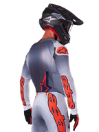 Motocross rider from behind wearing the Alpinestars 2025 Supertech Lipan Jersey in Gray Orange Fluo, featuring bold orange logos on the sleeves and back, paired with matching pants and a black helmet, professional racing outfit for off-road performance.