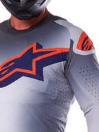 Alpinestars 2025 Supertech Lipan Jersey, Motocross Jersey, Gray Orange Fluo, featuring large navy and orange star logo on the chest, laser-cut perforations for airflow, lightweight mesh construction, worn with a black helmet
