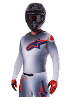 Motocross rider wearing Alpinestars 2025 Supertech Lipan Gear Set, Gray jersey and pants with navy and orange accents, matte black helmet with goggles, and red and black gloves, athletic performance gear for off-road racing