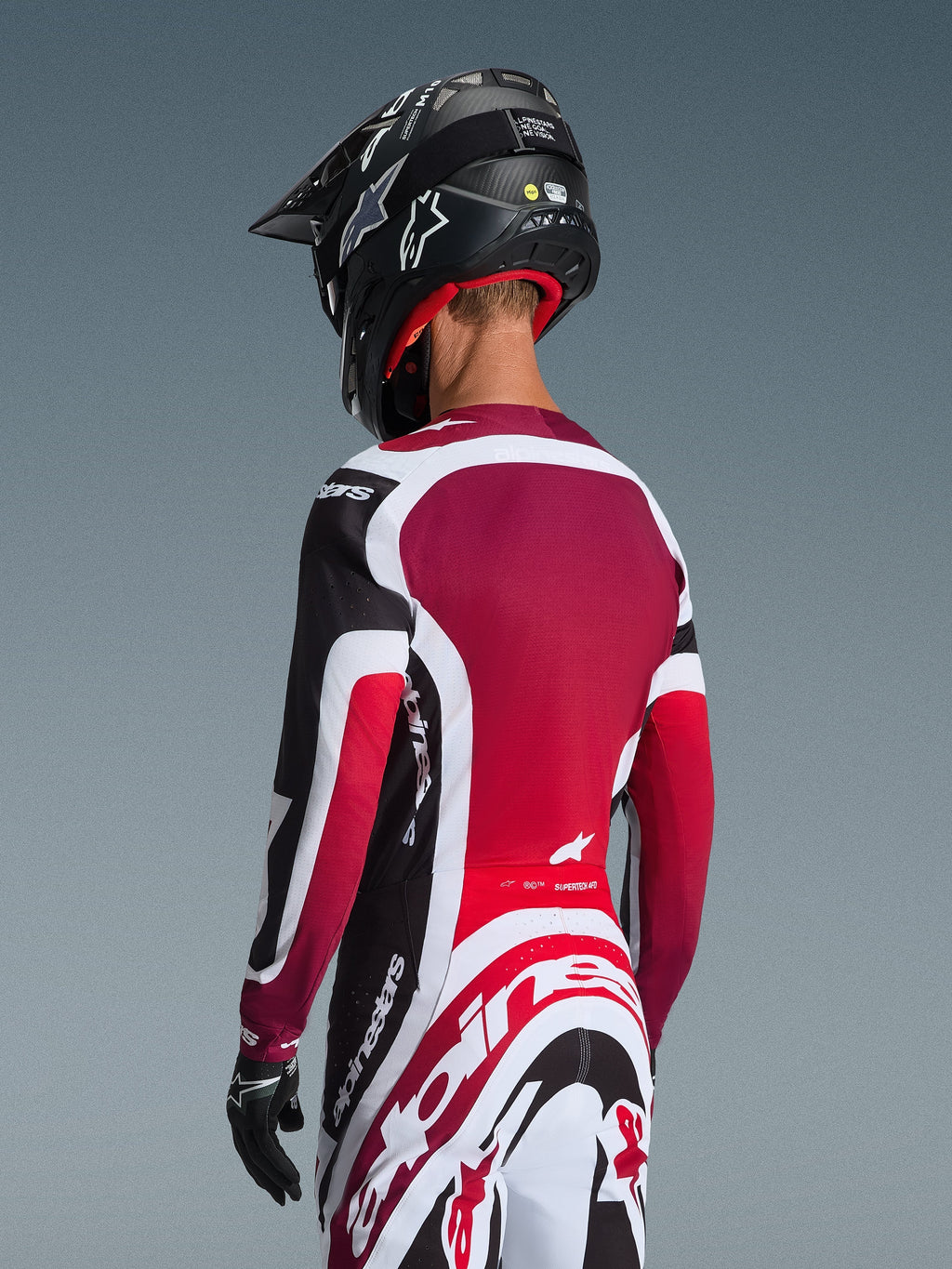 Alpinestars 2026 Supertech AFD Vista Gear Set, back view of a motocross rider in black, red, and white racing apparel, jersey with deep red back panel and athletic fit, matching pants with bold Alpinestars logo, black helmet and gloves, professional motocross racing outfit