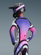 Motocross rider wearing the Alpinestars 2026 Supertech AFD Vista Jersey in White Purple and Black, back view showing a purple-to-pink gradient design, paired with matching pants and a black helmet, professional off-road racing gear.