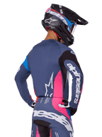 Motocross rider viewed from behind wearing the Alpinestars 2025 Techstar Dreem gear set in Gray, featuring a blue-gray jersey and pants with pink and black panels, white Alpinestars logos on the sleeves and back, and a matching black helmet with blue and pink graphics.