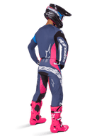 Motocross rider from a rear view, wearing the Alpinestars 2025 Techstar Dreem gear set, Gray with vibrant pink and white accents, black and white helmet, and bright pink boots, complete racing outfit for motocross performance.