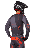 Alpinestars 2025 Racer Hollow Jersey, back view of a motocross rider in Gray Camo and Orange Fluo gear, featuring matching camo pants with large orange Alpinestars lettering and a black helmet, professional off-road apparel design