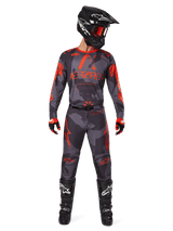 Motocross rider wearing Alpinestars 2025 Racer Hollow Jersey and matching pants in Gray Camo Orange Fluo, complete gear set with black helmet, goggles, gloves, and boots, featuring bold orange logos and camo pattern.