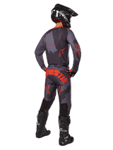Motocross rider from a rear view wearing the Alpinestars 2025 Racer Hollow Jersey in Gray Camo Orange Fluo, matching camo pants with orange Alpinestars text, black helmet, and black boots, coordinated gear set for off-road riding