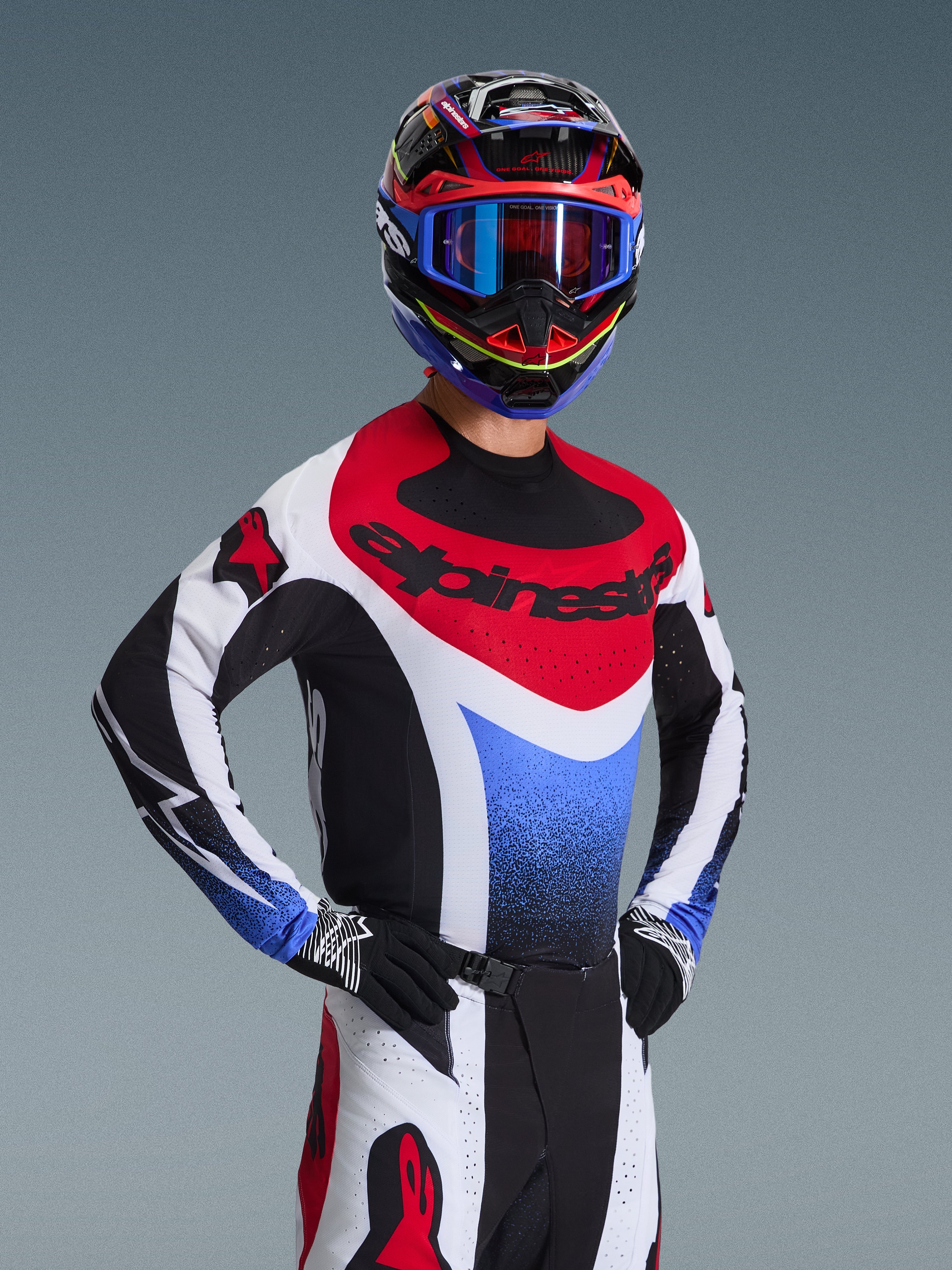 Alpinestars 2026 Techstar Knif Gear Set, Motocross rider in a red white and blue racing jersey with black accents, matching multi-color helmet and goggles, black gloves, professional gear for motocross competition.