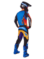 Motocross rider viewed from the back wearing Alpinestars 2025 Fluid Wurx Gear Set, multicolor jersey with blue orange and purple panels, matching pants with white Alpinestars logo on the seat, bright blue boots and a black helmet, coordinated outfit for off-road racing