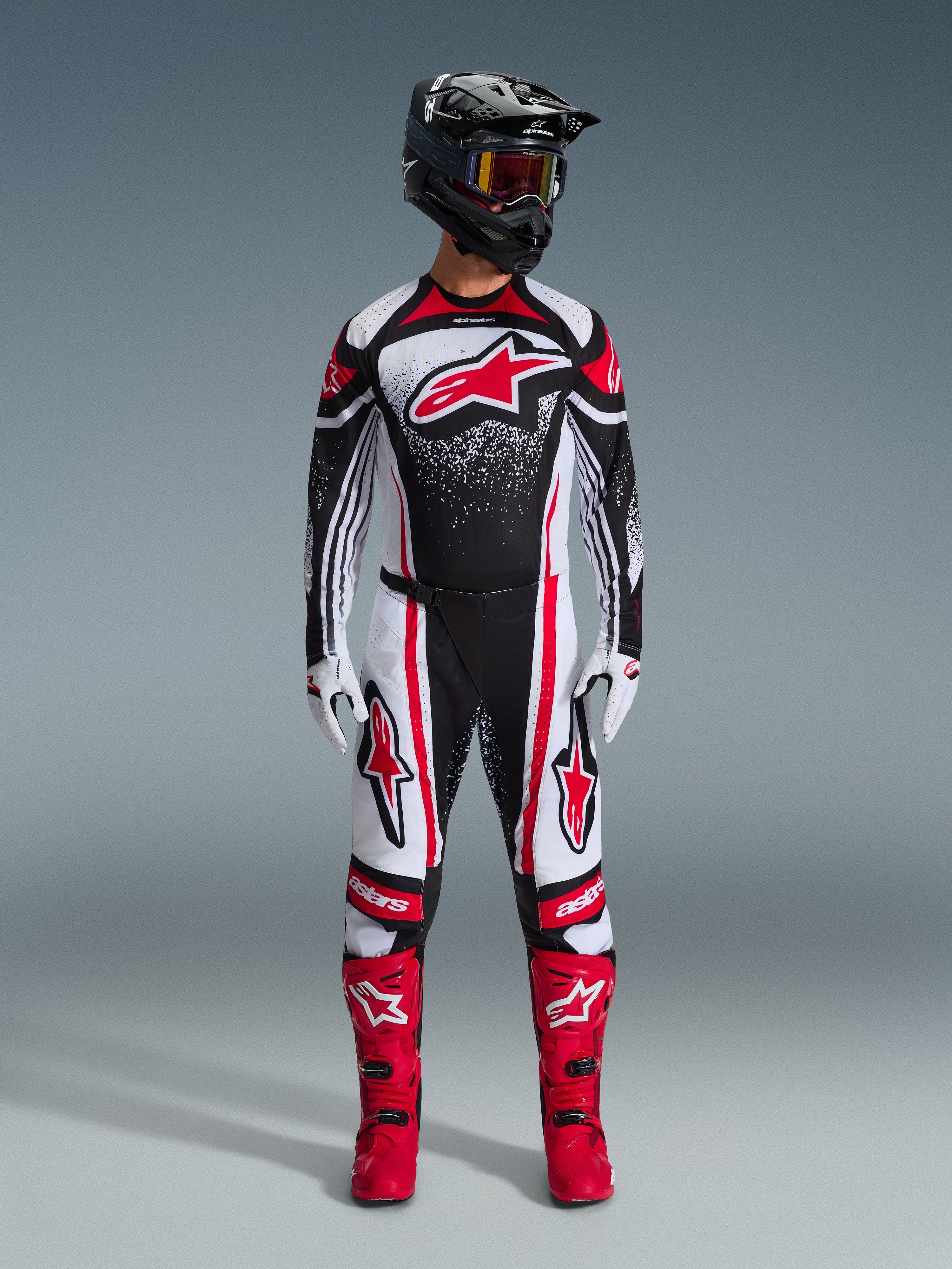 Motocross rider wearing the 2026 Techstar Nomur Gear Set, Black White and Red, jersey featuring a large red star logo and speckled pattern, matching pants with red side panels, black helmet with tinted goggles, and red motocross boots.