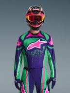 Alpinestars 2026 Techstar Nomur Gear Set, Motocross rider wearing vibrant green and purple racing jersey with pink accents, matching gear set with multi-colored helmet and goggles, high-performance off-road motorcycle outfit