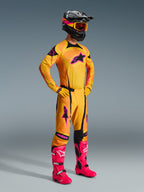 Motocross rider wearing the 2026 Techstar Nomur Jersey in Orange Yellow and Pink, matching orange pants with pink accents, bright pink boots, yellow gloves, and black helmet with yellow goggles, coordinated motocross racing gear set