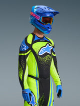 Motocross rider wearing the 2026 Techstar Nomur Jersey in Dark Navy and Yellow Fluo, paired with matching pants, a blue racing helmet, and goggles, featuring a large Alpinestars logo and athletic race fit for off-road performance.