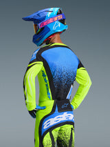 Motocross rider wearing Alpinestars 2026 Techstar Nomur Jersey, Yellow Fluo and Blue, back view showing athletic race fit and moisture-wicking fabric, paired with matching pants and blue helmet, complete professional off-road racing gear