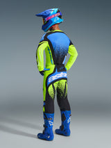 Motocross rider from behind wearing complete racing gear, 2026 Techstar Nomur Jersey in yellow fluo and blue, matching yellow and black pants with blue accents, blue helmet with pink Alpinestars logo, and blue boots, studio shot highlighting the back design and athletic fit.